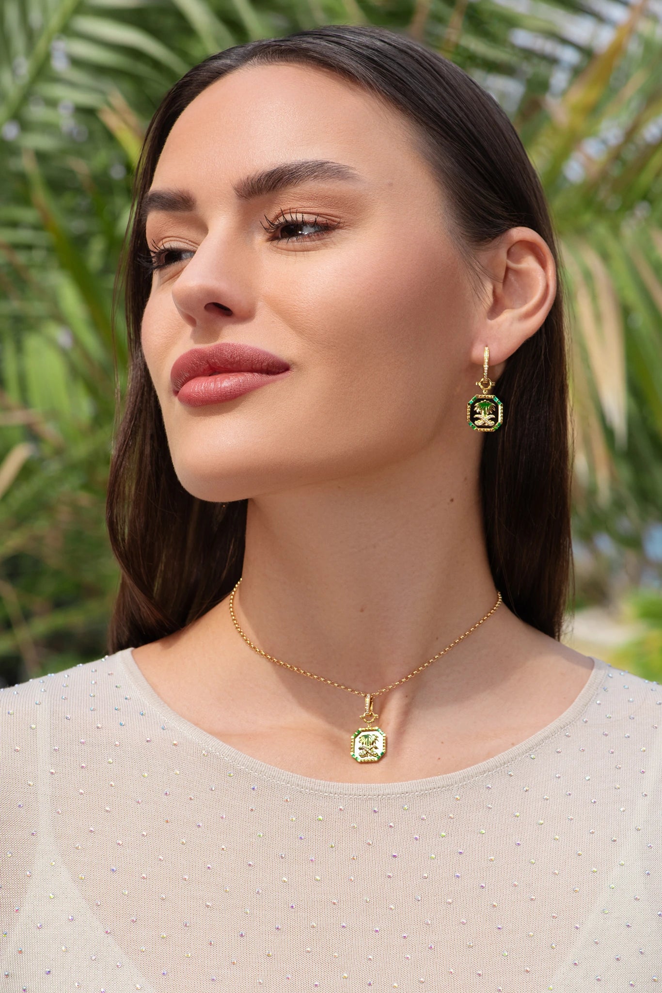 Woman wearing gold jewelry with green gemstones against a blurred natural background