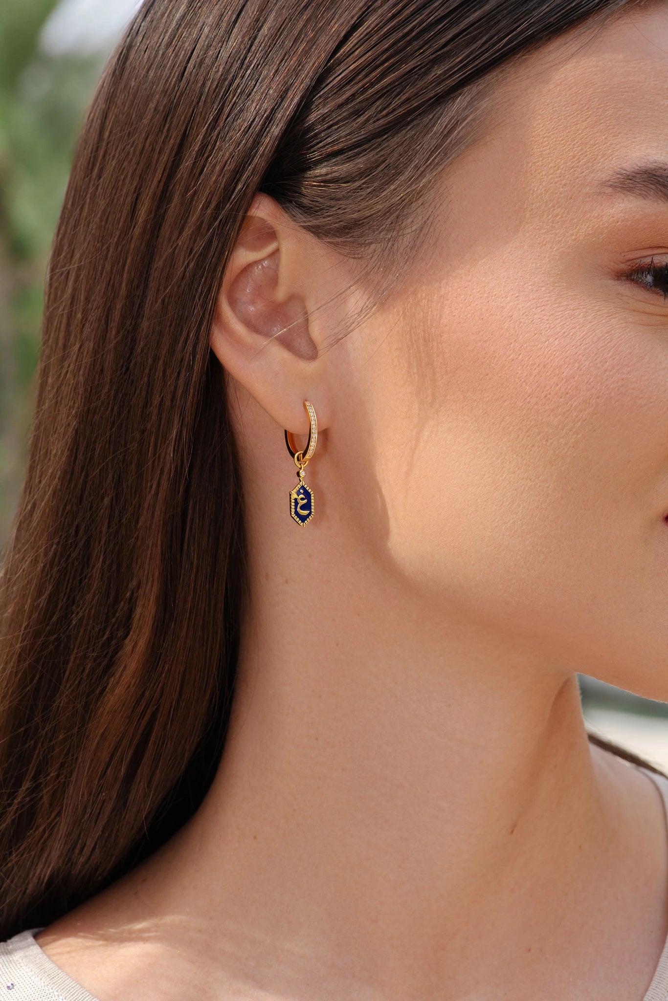 Close-up of a person wearing gold hoop earrings with a small black heart pendant.