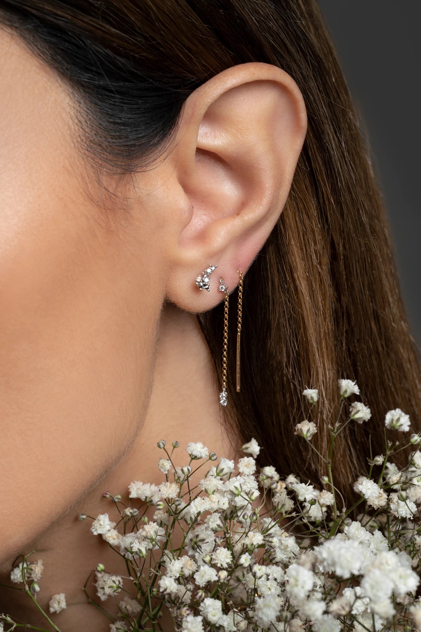 Close-up of an ear wearing a delicate earring with flowers in the foreground